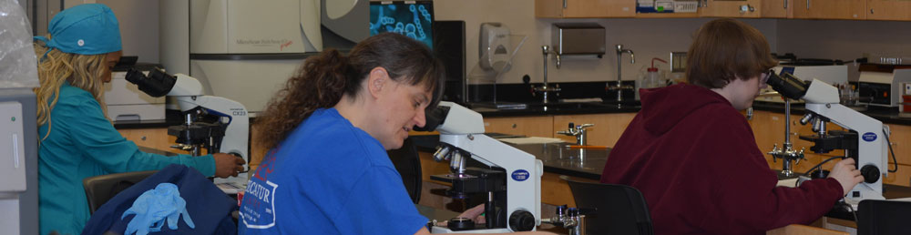 Three students sitting at microscopes in a med lab classroom