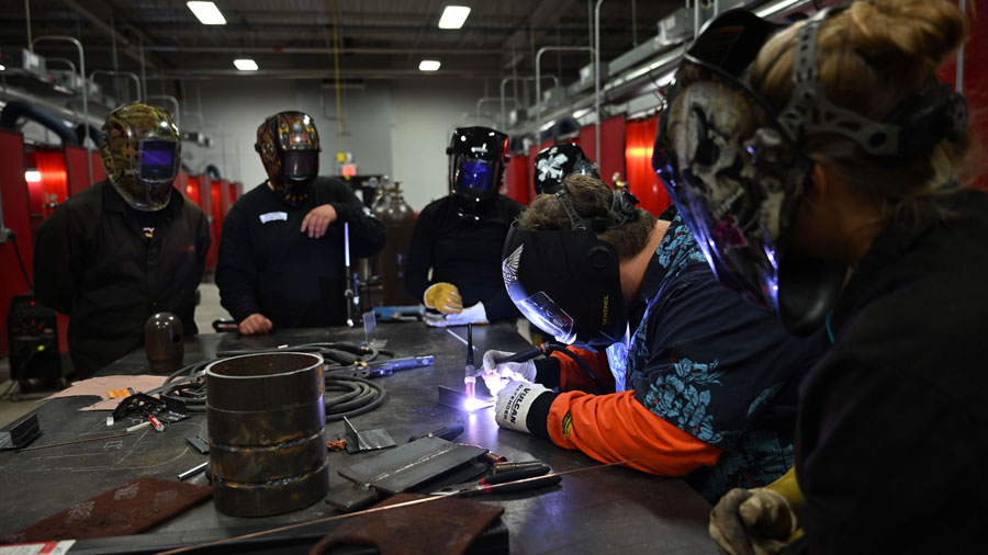 Instructor doing a TIG welding demonstration with four students watching in personal protective equipment