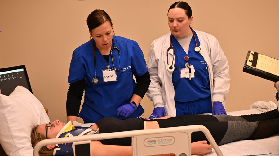 Student in a medical bed and two students doing a training exercise
