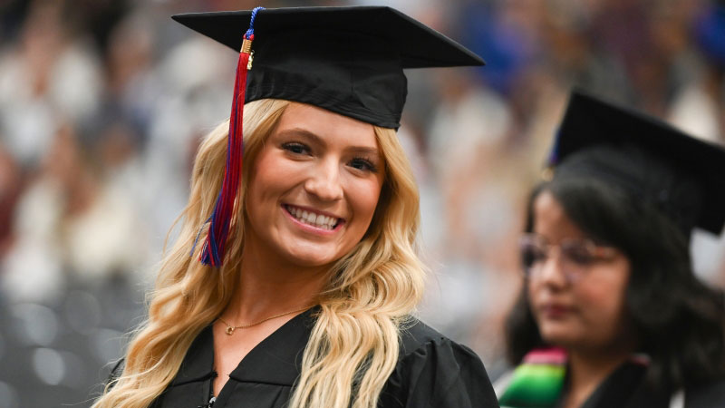 A student in Cap and gown smiling at the camera during the ceremony.